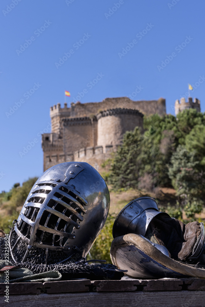 Close-up of a helmet and protective gloves for medieval combat, and in the background a castle