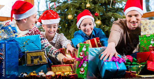 Mum, dad and sons on X-mas during handing out of presents under Christmas tree