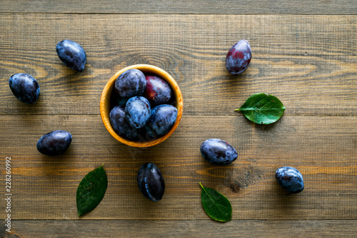 Plums on dinning table. Fresh raw purple plum in wooden bowl on wooden background top view copy space