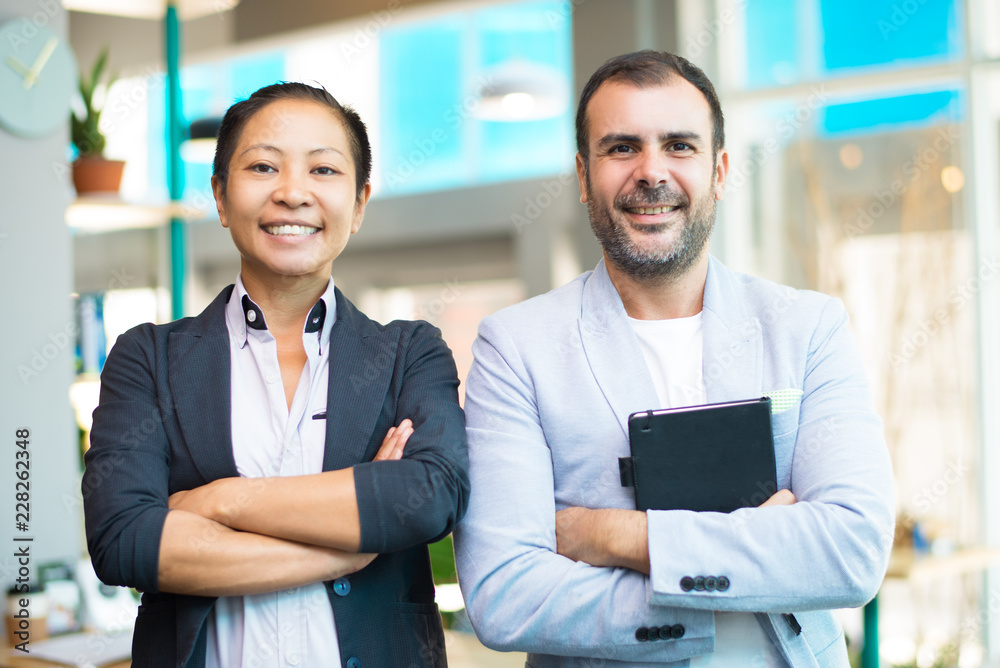 Happy Asian and Latin managers looking at camera with crossed arms ...