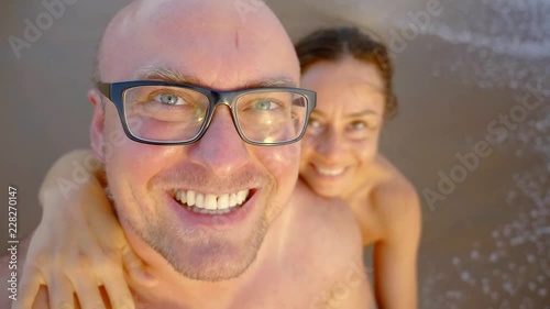 cheerful bald man and his woman are taking selfie on a camera on a wild beach near sea photo