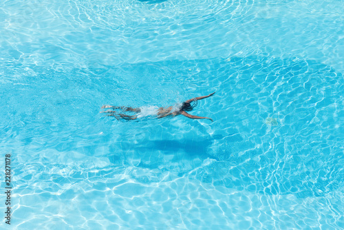 Aerial view on the men in the swimming pool with transparent blue water. In the motion