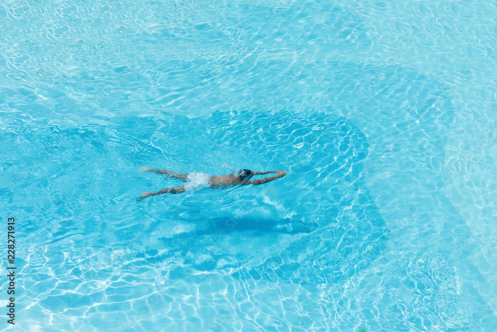 Aerial  view on the men in the swimming pool with transparent blue water. In the motion