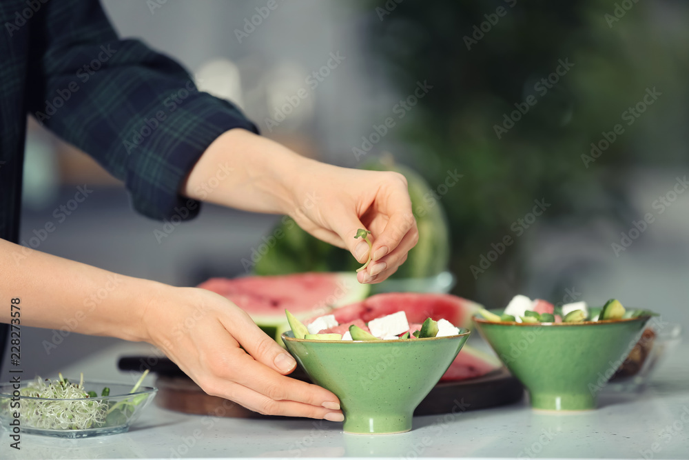 Woman preparing tasty salad with watermelon in kitchen