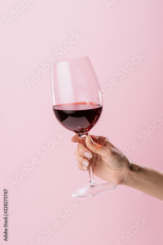 cropped shot of woman holding glass of red wine isolated on pink
