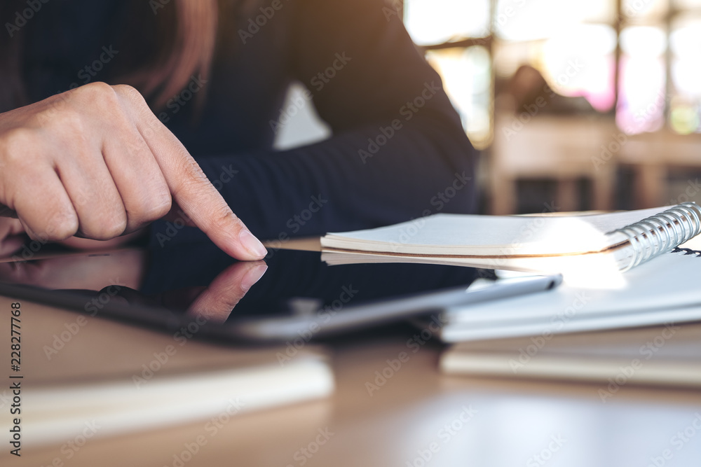 Closeup image of hand pointing at a black tablet pc screen with notebook on wooden table