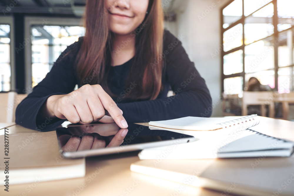 Closeup image of an asian woman pointing at a black tablet pc screen with notebook on wooden table Closeup image of an asian woman pointing at a black tablet pc screen with notebook on wooden table