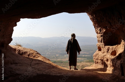 MAN WITH DJELLABA LOOKING TO THE VALLEY FROM A HIGH CAVE photo