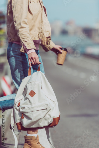 partial view of female traveler with backpack and coffee to go crossing road in new city