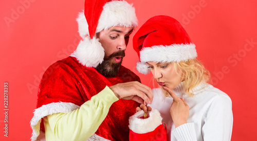 Couple cheerful face check out gift in christmas sock. Woman and bearded man in santa hat expecting gift red background. Check contents of christmas stocking gift received. Christmas gift concept