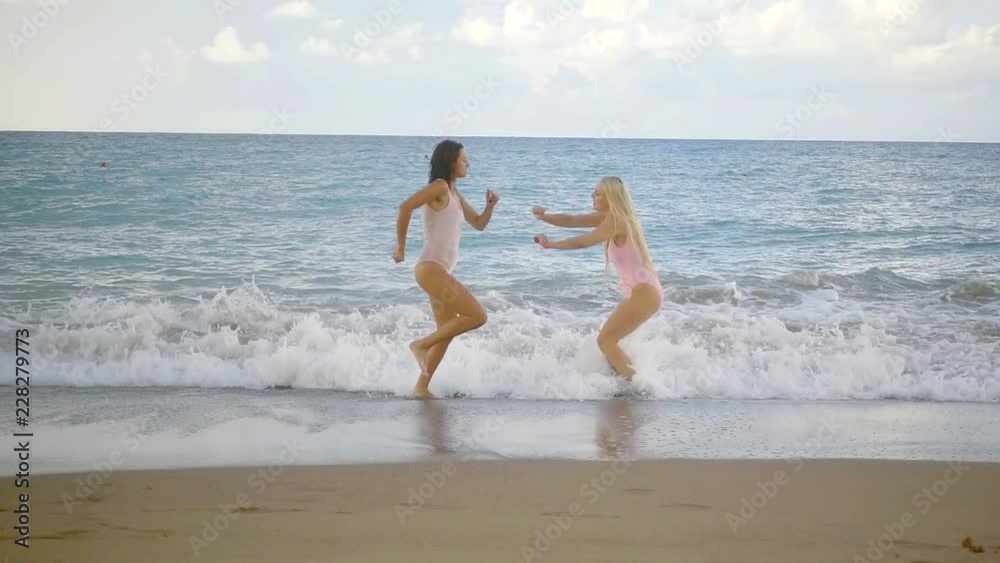 two sporty women are leaping and running in ocean waves in tidal time, slow motion shot two sporty women are leaping and running in ocean waves in tidal time, slow motion shot