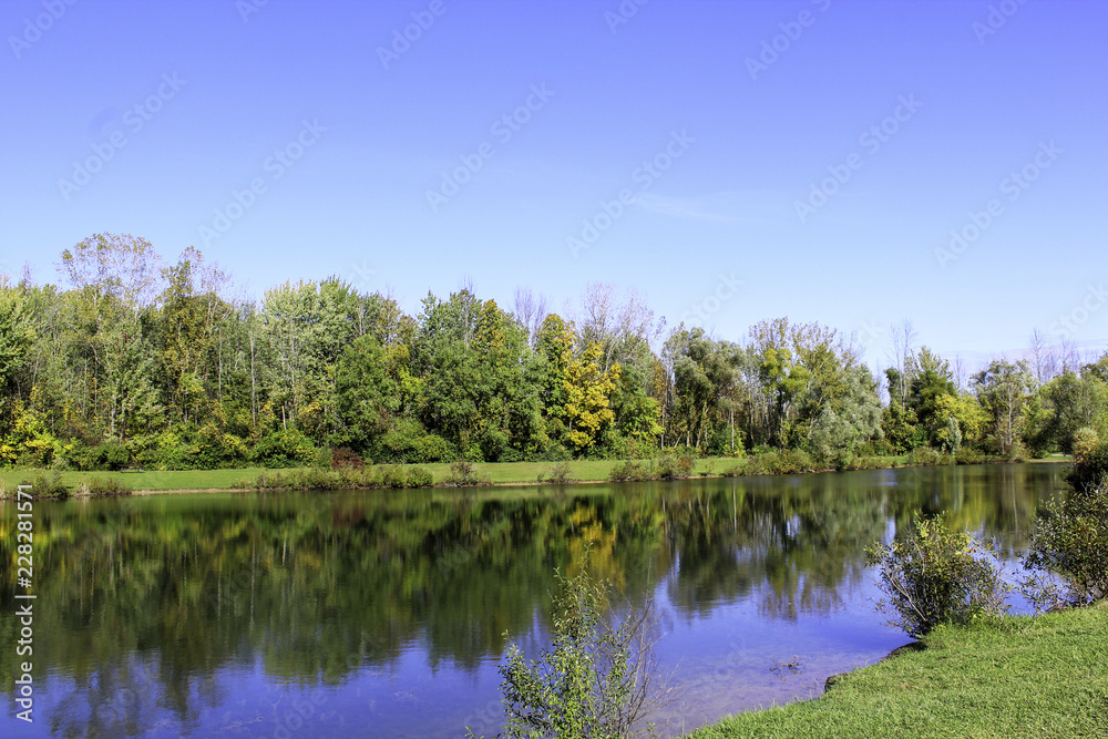 Obraz premium Autumn foliage reflections on calm blue pond. Rochester, New Yorl