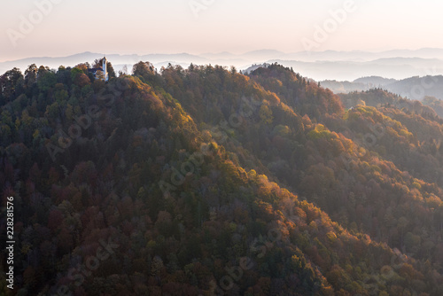 Church on top of rolling forest hills in autumn colors illuminated with soft sunlight early morning 