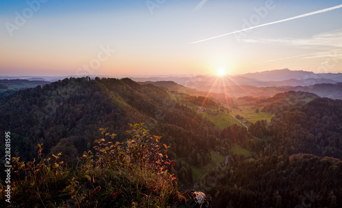 Colorful tranquil sunrise behind Swiss Alps in autumn viewed from a high angle view with a valley and rolling hills in the scene 