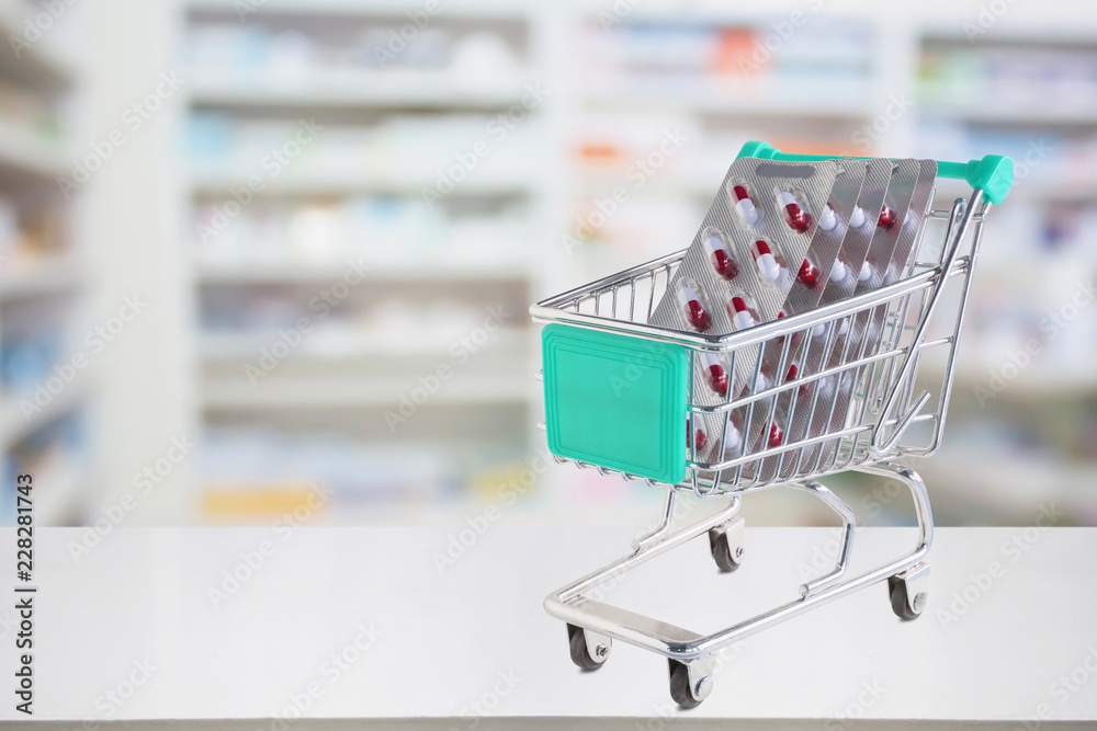 medicine pills capsule in shopping cart on pharmacy store counter with blur drugstore shelves defocused background medicine pills capsule in shopping cart on pharmacy store counter with blur drugstore shelves defocused background