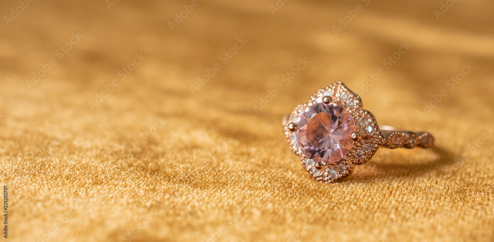 Obraz premium Jewelry pink diamond ring on golden fabric background close up