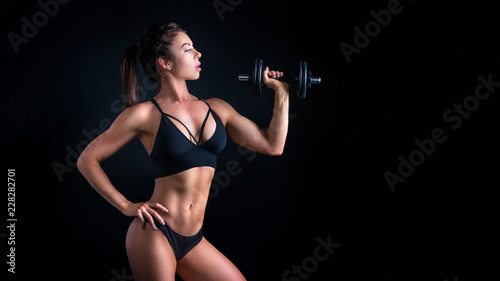 Brutal athletic woman pumping up muscles with dumbbells.