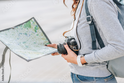 cropped view of traveler holding photo camera and map in city