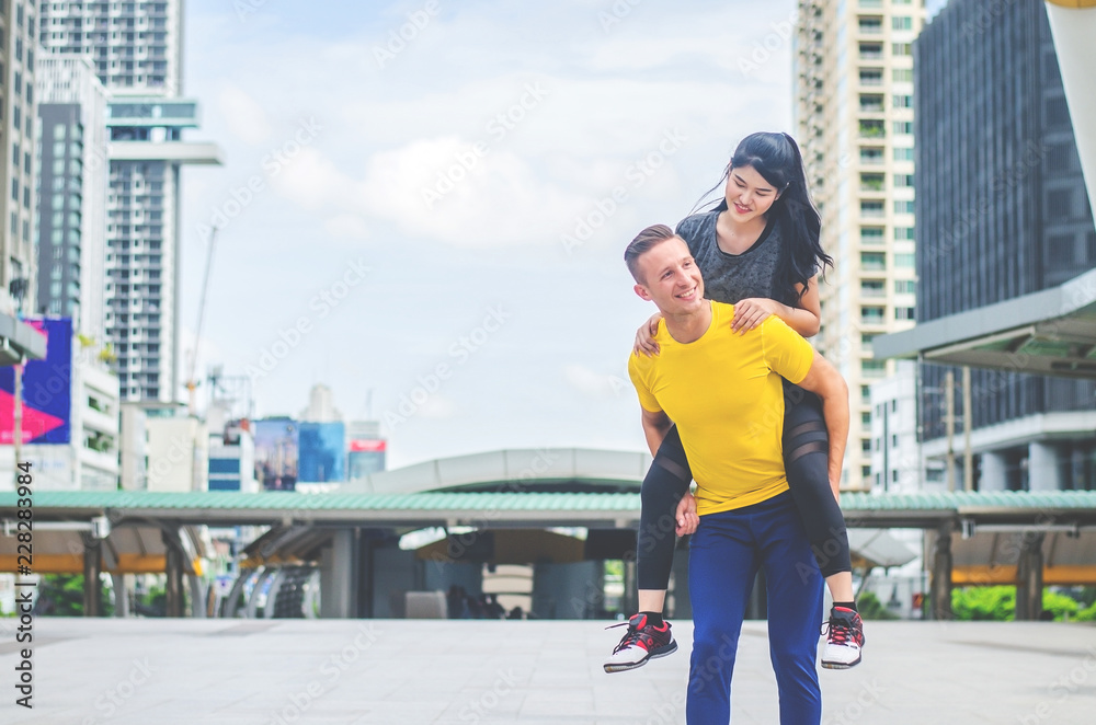 Happy sport man carrying his woman on back at the city background Happy sport man carrying his woman on back at the city background
