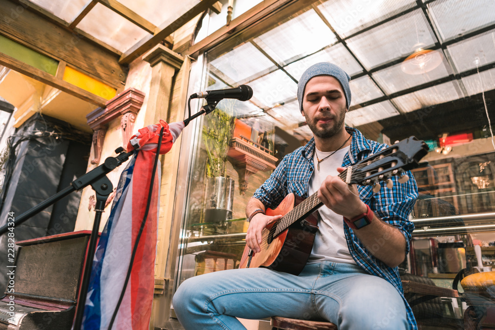 Professional guitarist. Low angle of focused male guitarist staring in fingerboard and playing song Professional guitarist. Low angle of focused male guitarist staring in fingerboard and playing song