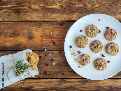 Selbstgemachte Weihnachts Cranberry Kekse mit Zuckerguss verziert auf einem weißen Teller und eine Papiertüte mit Keksen 