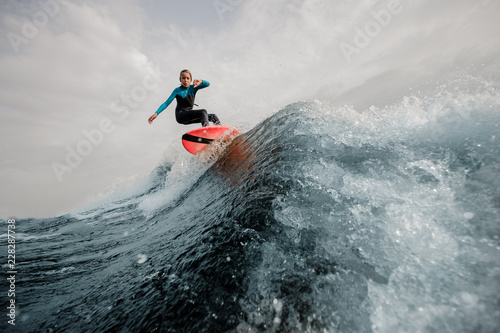 Active boy dressed in swimsuit wakesurfing jumping up on orange board