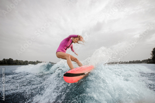 Blonde woman wakesurfer riding down the blue splashing wave