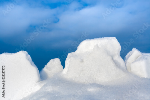 Close-up white snow lumps against blue sky. 