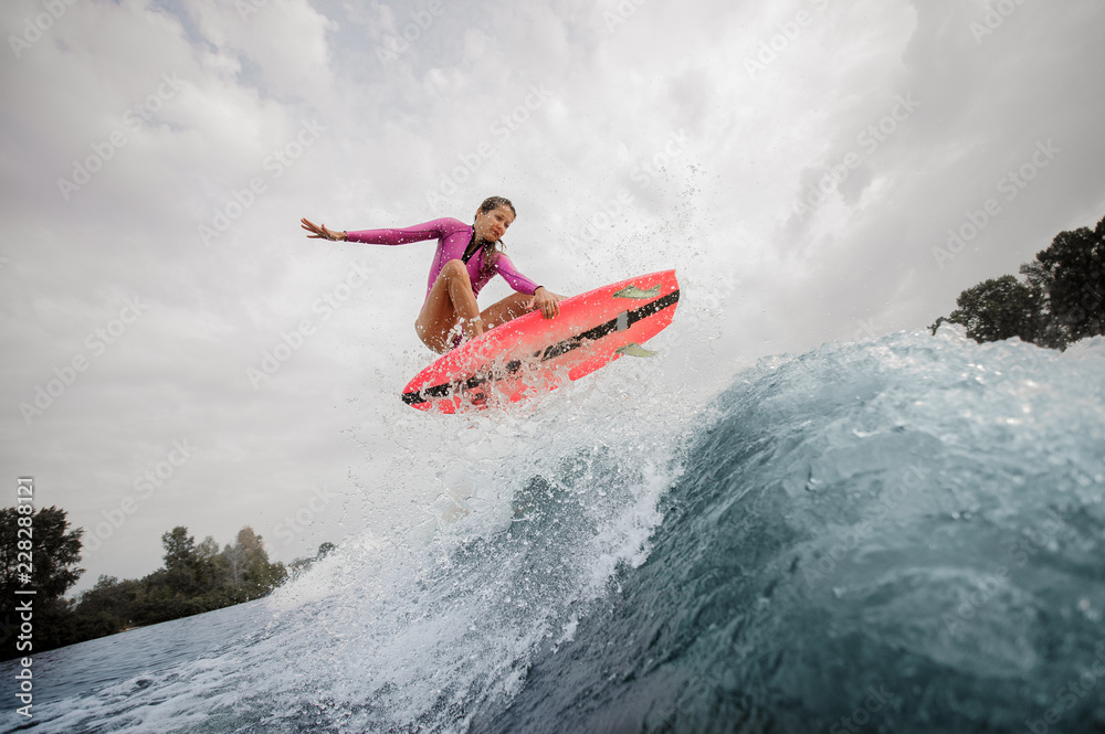 Active and young woman wakesurfer jumping up the blue splashing wave against sky