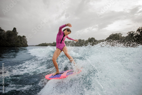Woman wakesurfer riding down the blue splashing river against sky