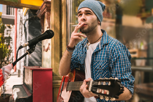 Bad habit. Musing male guitarist smoking cigarette and carrying guitar