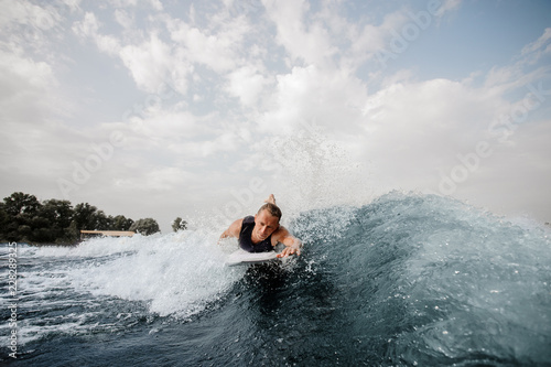 Handsome wakesurfer lying on white board and swimming down the river