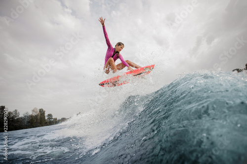 Active teenager girl in the pink swimsuit jumping on the orange wakeboard
