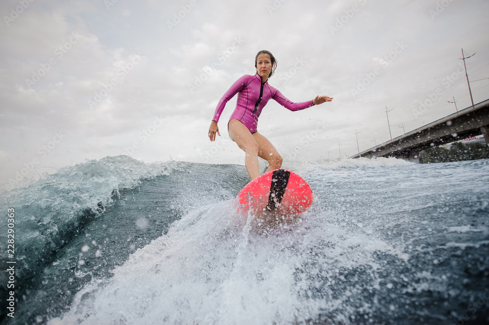 Attractive teenager girl in pink swimsuit riding on the orange wakeboard