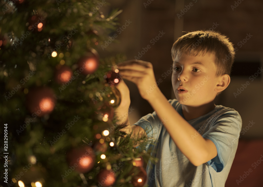 Cheerful boy decorating his Christmas tree at home Cheerful boy decorating his Christmas tree at home