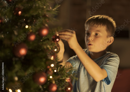 Cheerful boy decorating his Christmas tree at home