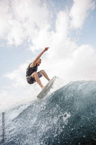 Young active man jumping up on the white wakeboard on the high wave