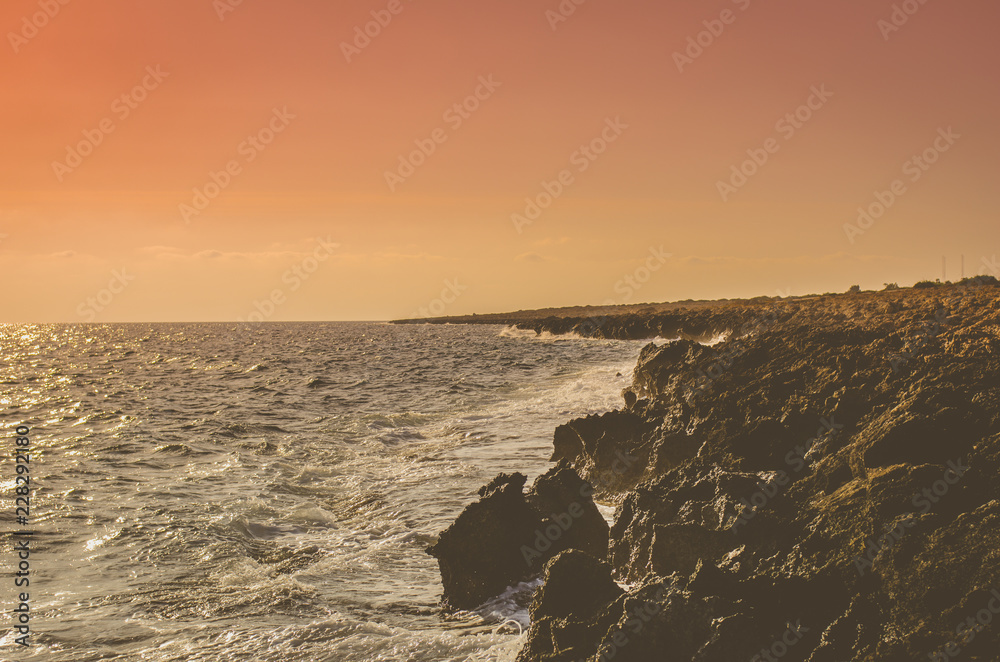Rocky coast with sharp edges, washed by the ocean on a background of red sky