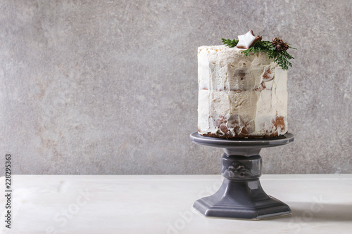 Christmas homemade white naked cake decorated by rated by star cookie and green thuja branches on cake stand on white marble table with grey wall at background. Minimalist style. Copy space