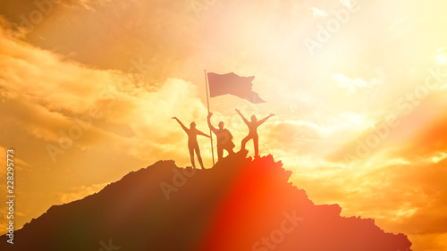 Tablou pe pânză High achiever, silhouettes of three people holding on top of a mountain to raise their hands up