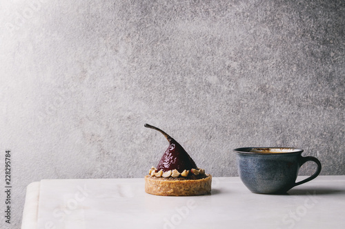 Fotografi Sweet red wine tartlet with cup of coffee espresso standing on white marble table with grey wall at background