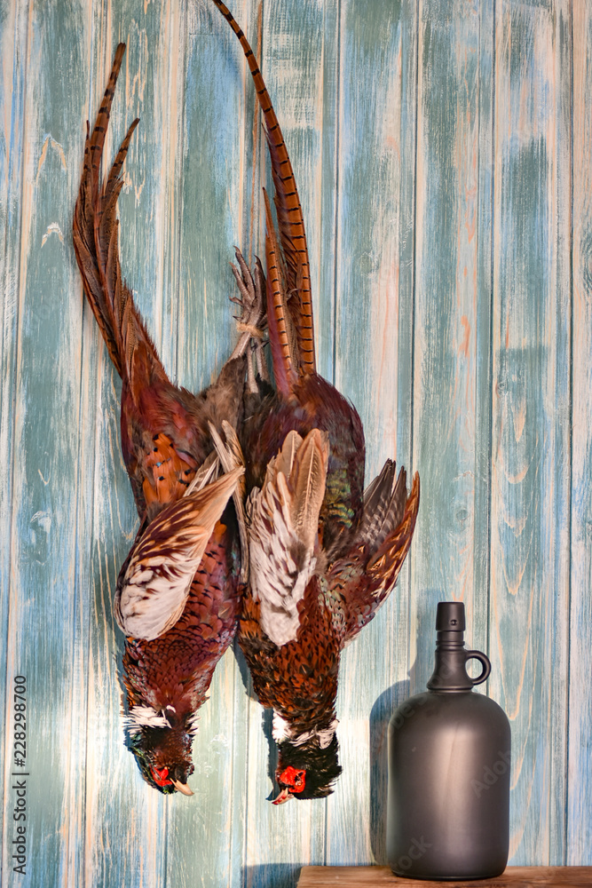 Fototapeta premium A pair of Male Pheasants and boottle on a old wooden background. Hunting season. Copy paste. Full size