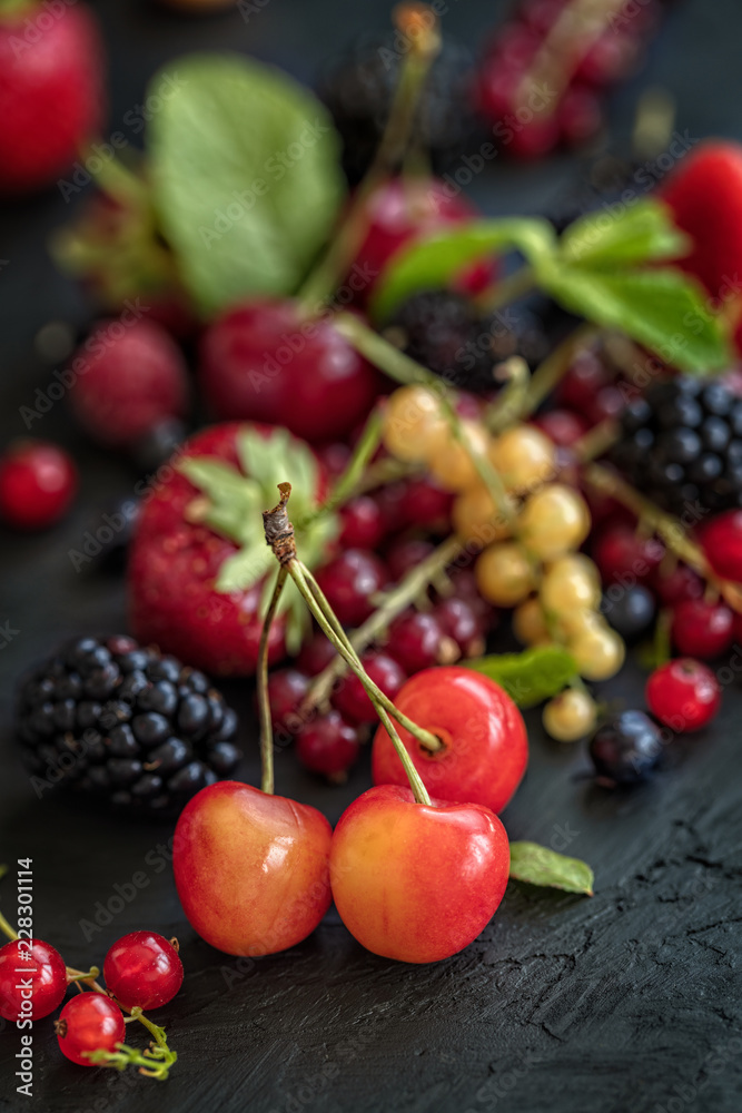 Mixed berries on a dark background with selected focus. Strawberries, Raspberries Blackberries, cherries, red and yellow currents. Healthy Living and Nutritious Food concept. Vertical composition Mixed berries on a dark background with selected focus. Strawberries, Raspberries Blackberries, cherries, red and yellow currents. Healthy Living and Nutritious Food concept. Vertical composition