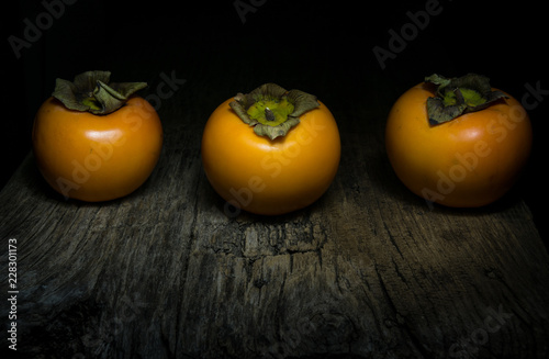 tre cachi mela/diosperi su tavolo di legno con luce da studio e sfondo nero, tecnica del light painting photo