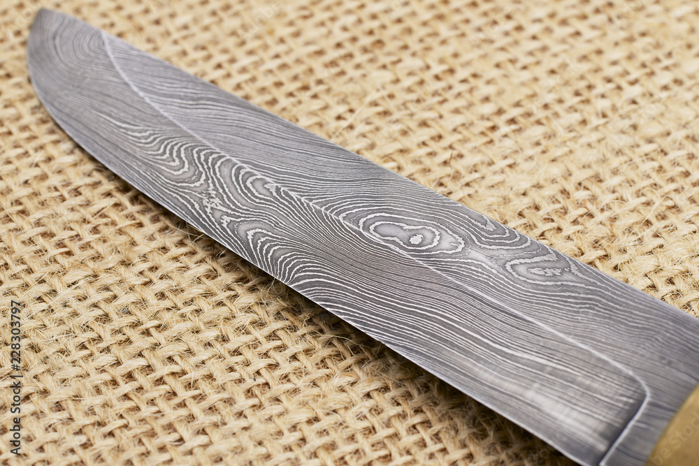 Traditional handmade Finnish knife with the abstract wave pattern of damascus  steel over an old sack background. Stock-bilde | Adobe Stock