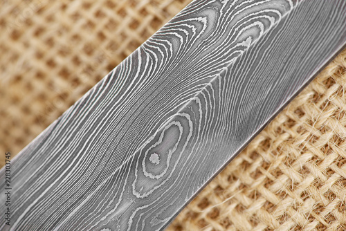 Traditional handmade Finnish knife with the abstract wave pattern of damascus steel over an old sack background.