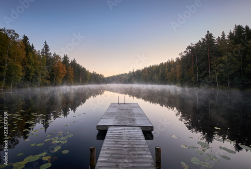 Scenic and idyllic lake landscape with pier and fog at autumn morning in Finland