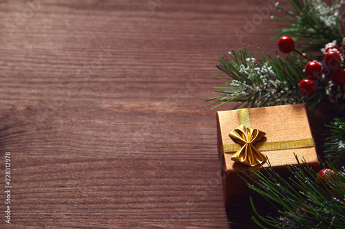 Fir tree branches, red berries and present box on wooden surface. Christmas and new year background.