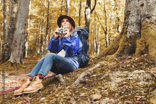 Young beautiful woman wearing hat and blue cloak with walking sticks in a forest, having a break, shooting, travel lifestyle success concept adventure active summer vacations outdoor mountaineering
