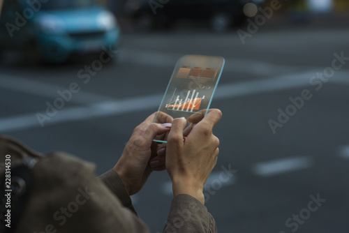 Close up on a female hand that is holding a transparent phone gadget concept, using an app that displays data and statistic graphic charts